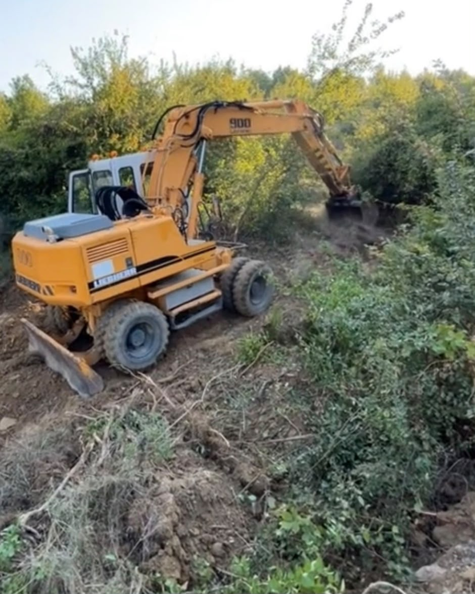 Ekskavator i verdhë që punon në një pjerrësi të mbushur me shkurre