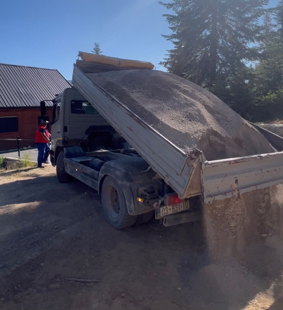 Kamioni me shkarkim hapur derdh material pranë një shtëpie me dru